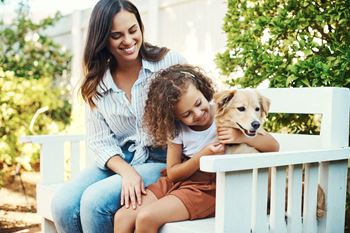 A woman and a child are sitting on a bench with a dog.